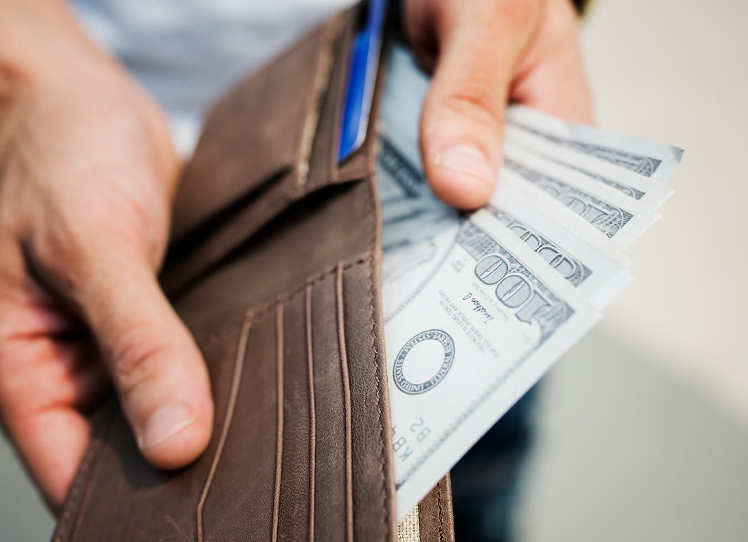 Hands holding an open wallet with several hundred-dollar bills
